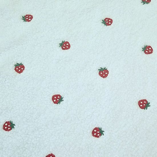 Kuschelig weicher Teddystoff in weiß mit kleinen Erdbeeren bestickt.