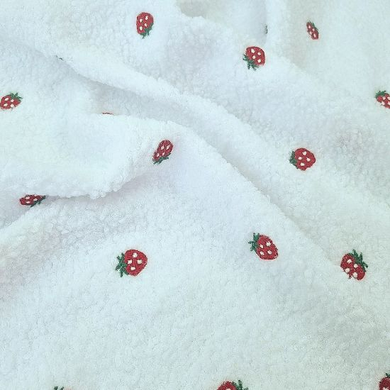 Kuschelig weicher Teddystoff in weiß mit kleinen Erdbeeren bestickt.